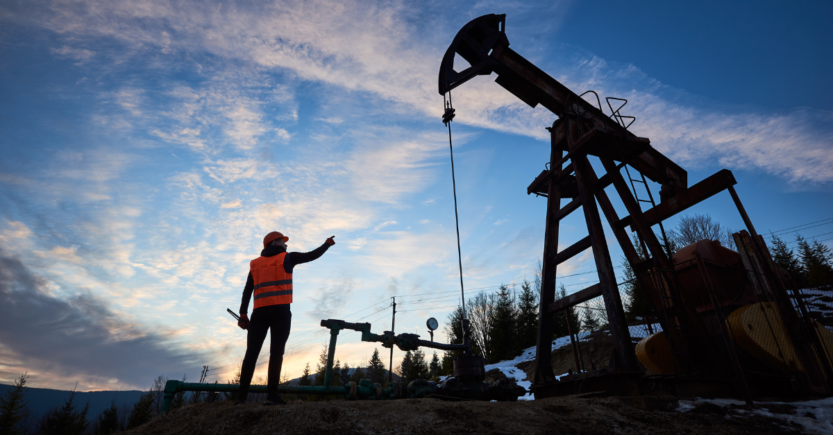 a person standing next to an oil pump at sunset